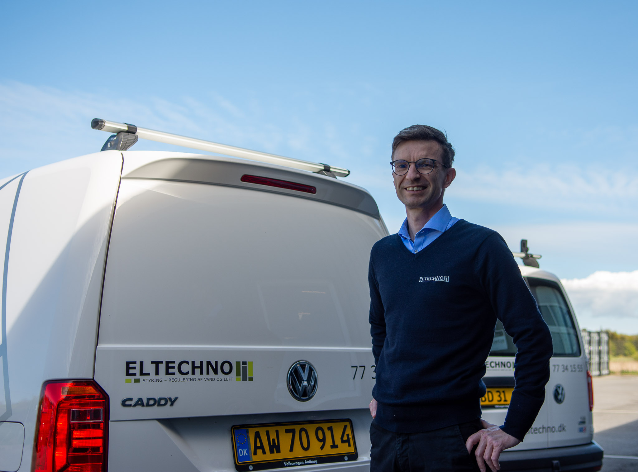 Billede af Morten Krogsgaard Nielsen der står ved to firmabiler fra ELTECHNO